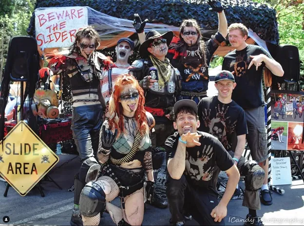 A group in costume poses at a themed event, flaunting "Slide Area" signs, representing the spirited Slider Team.