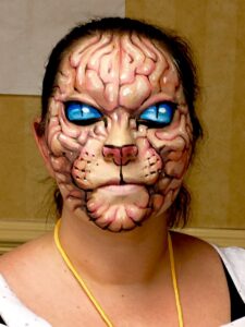 Person with intricate feline face paint, blue eyes, and fur-like patterns showcases expert Dutch makeup application.