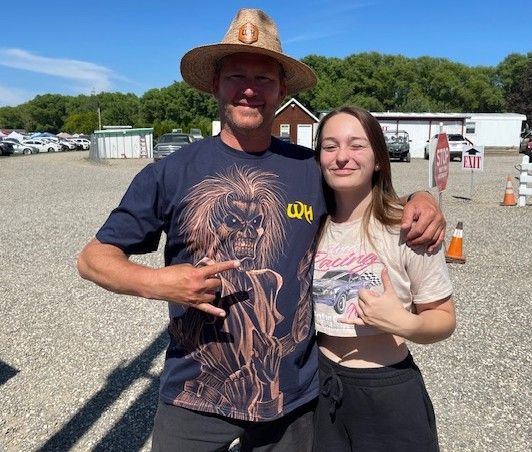 A man in a straw hat and Zayda smile and pose for a photo outside on a sunny day.