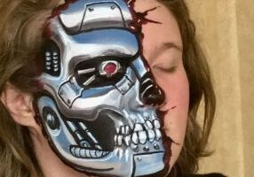 Dutch-inspired makeup application reveals a half-exposed robot skull, eyes closed, against a neutral background.