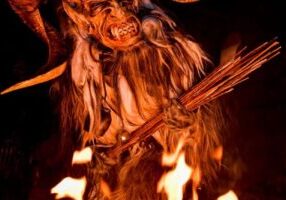 Krampus 2 A Bremerton Krampus in a horned costume stands behind flames, holding a bundle of sticks.