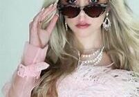 OIP 3 Woman with long blonde hair wearing sunglasses, a pink feathered top, and pearl jewelry, looking at the camera.