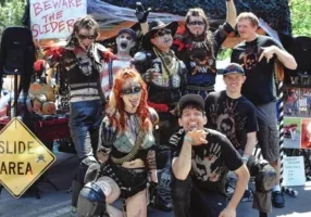 A group in costume poses at a themed event, flaunting "Slide Area" signs, representing the spirited Slider Team.