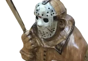 This is a wooden sculpture depicting a figure donned in a hockey mask and gripping a machete, designed in the manner of an iconic horror movie antagonist.