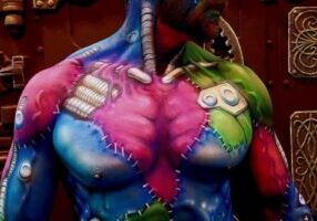 A Dutch man showcases a colorful Frankenstein-style body painting demo against a steampunk-themed background.