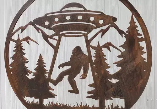 A metal wall art with a bigfoot flying over a forest.