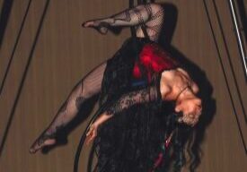 An artist is seen suspended upside down on aerial silks, donned in costume at Akasha Aerial Arts.